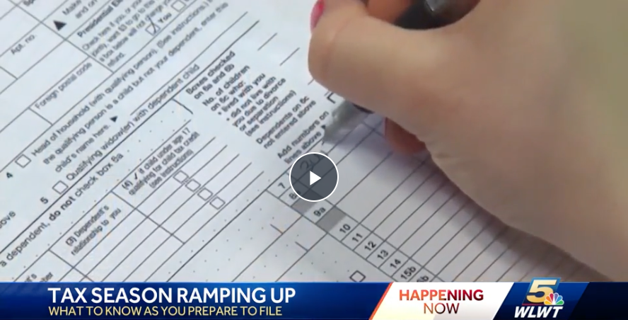 A close-up of a person’s hand holding a pen and filling out a tax form. The form contains various checkboxes and lines for entering information. A news banner at the bottom of the image reads "TAX SEASON RAMPING UP – WHAT TO KNOW AS YOU PREPARE TO FILE," with the WLWT 5 logo and "HAPPENING NOW" displayed.